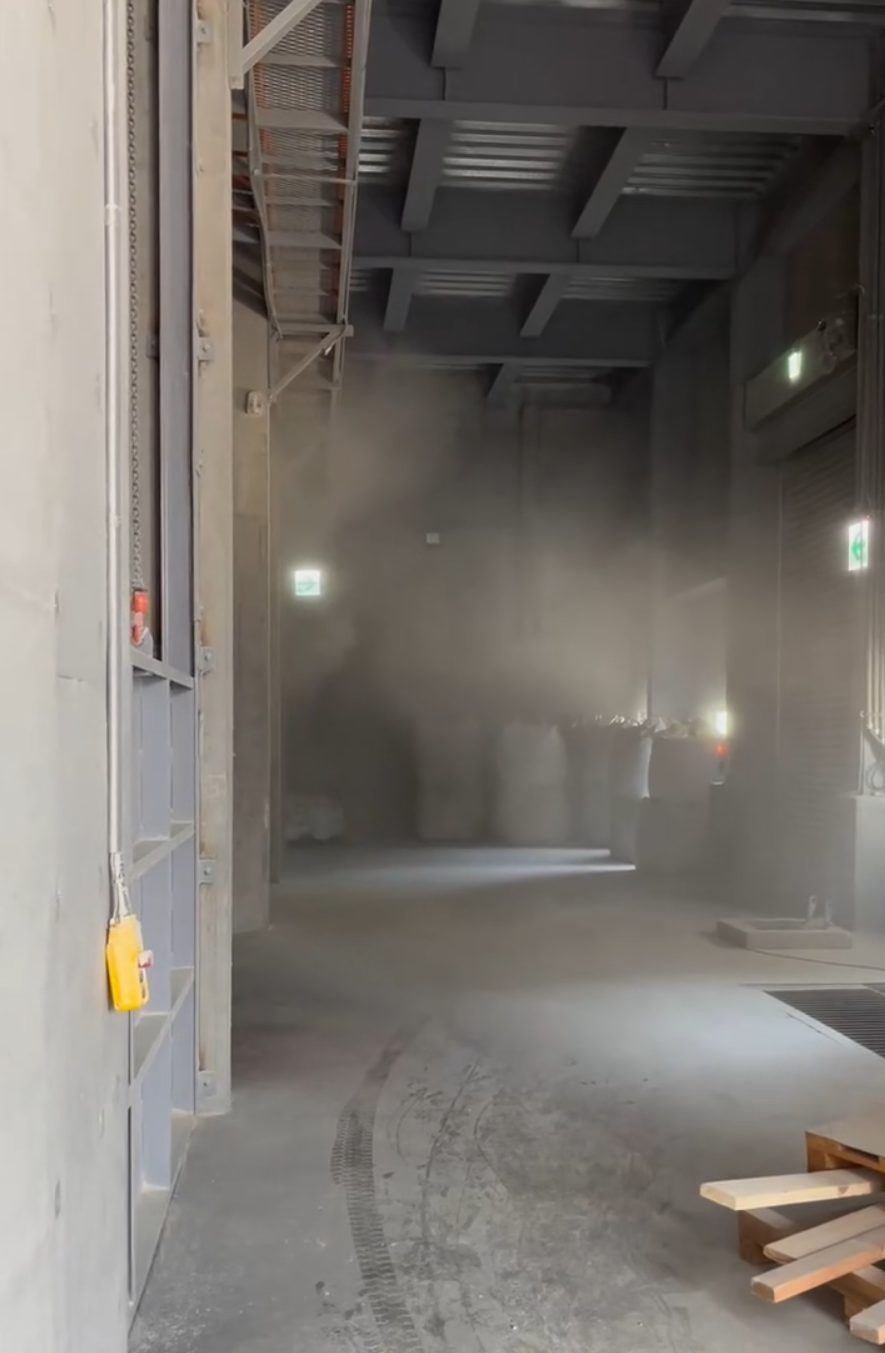 Dust drifting out of a bay opening into an adjacent area where bulk bags are stored
